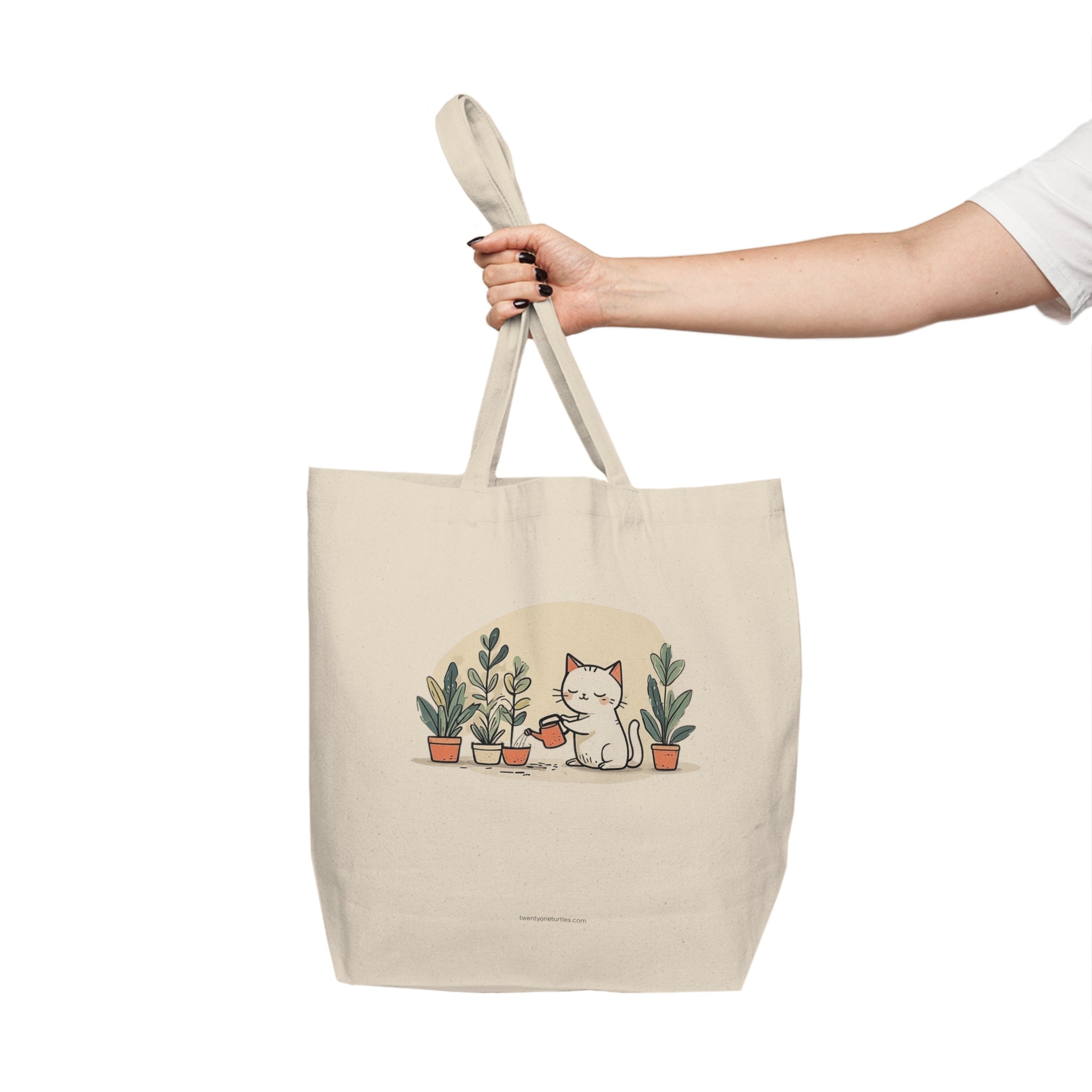 Beige tote bag with a cat and plants design held by a hand on a white background