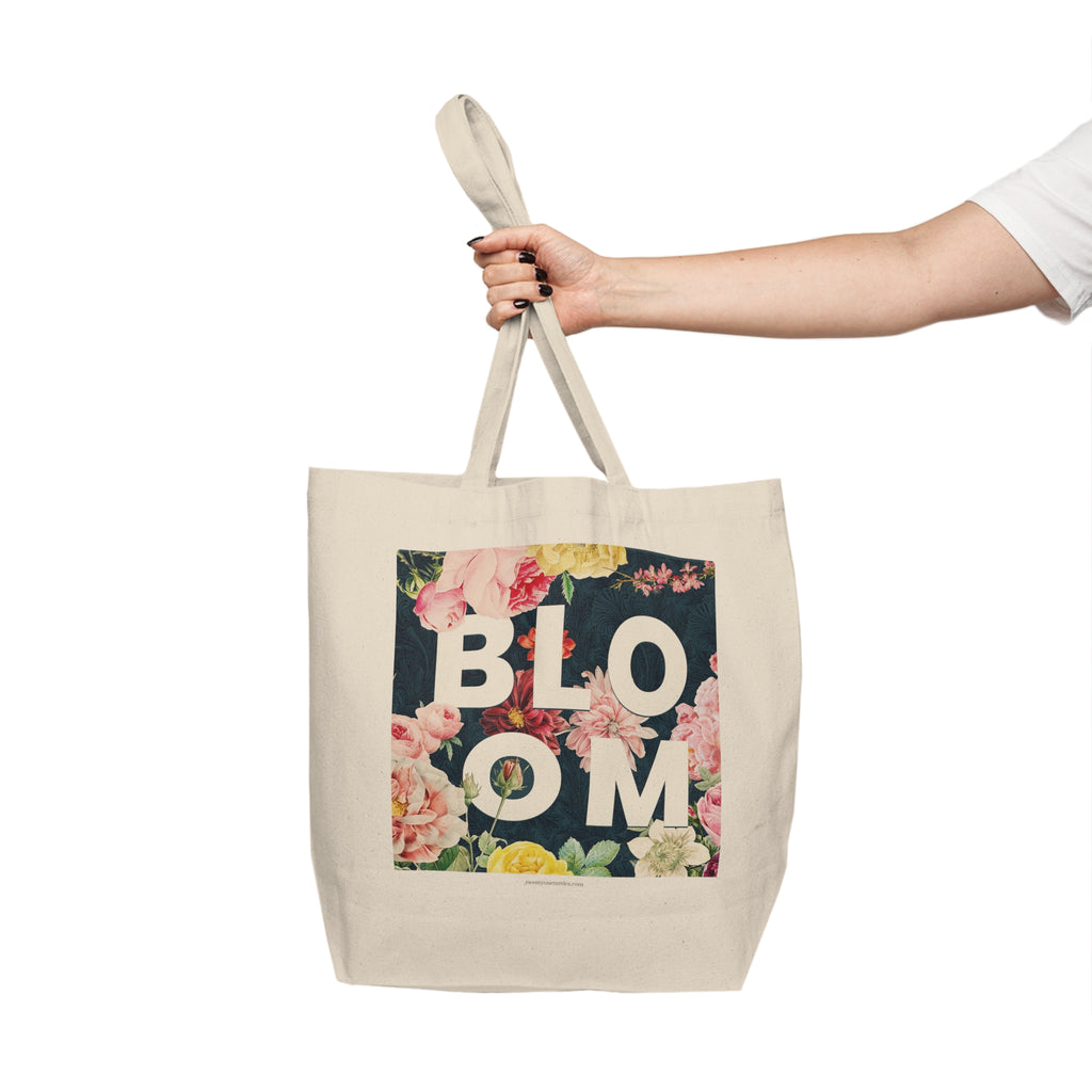 Tote bag with floral design and 'BLOOM' text held by a hand on a white background