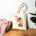Floral tote bag on a wooden surface with a white wall and plant in the background