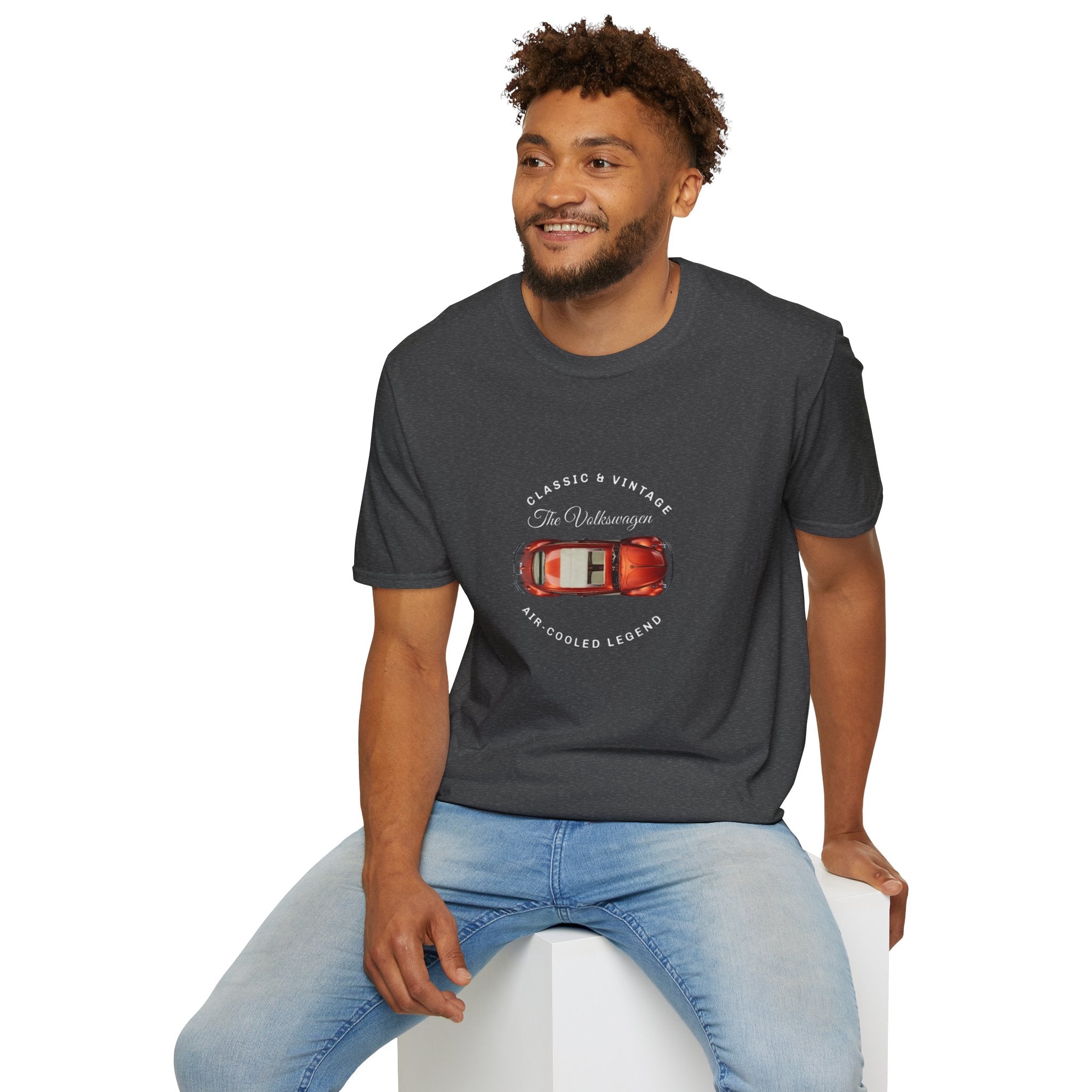 Man wearing a dark gray t-shirt with a red VW car graphic and text, sitting on a white stool against a white background.