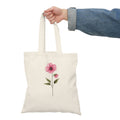 Tote bag with a pink flower design held by a person wearing a denim jacket.