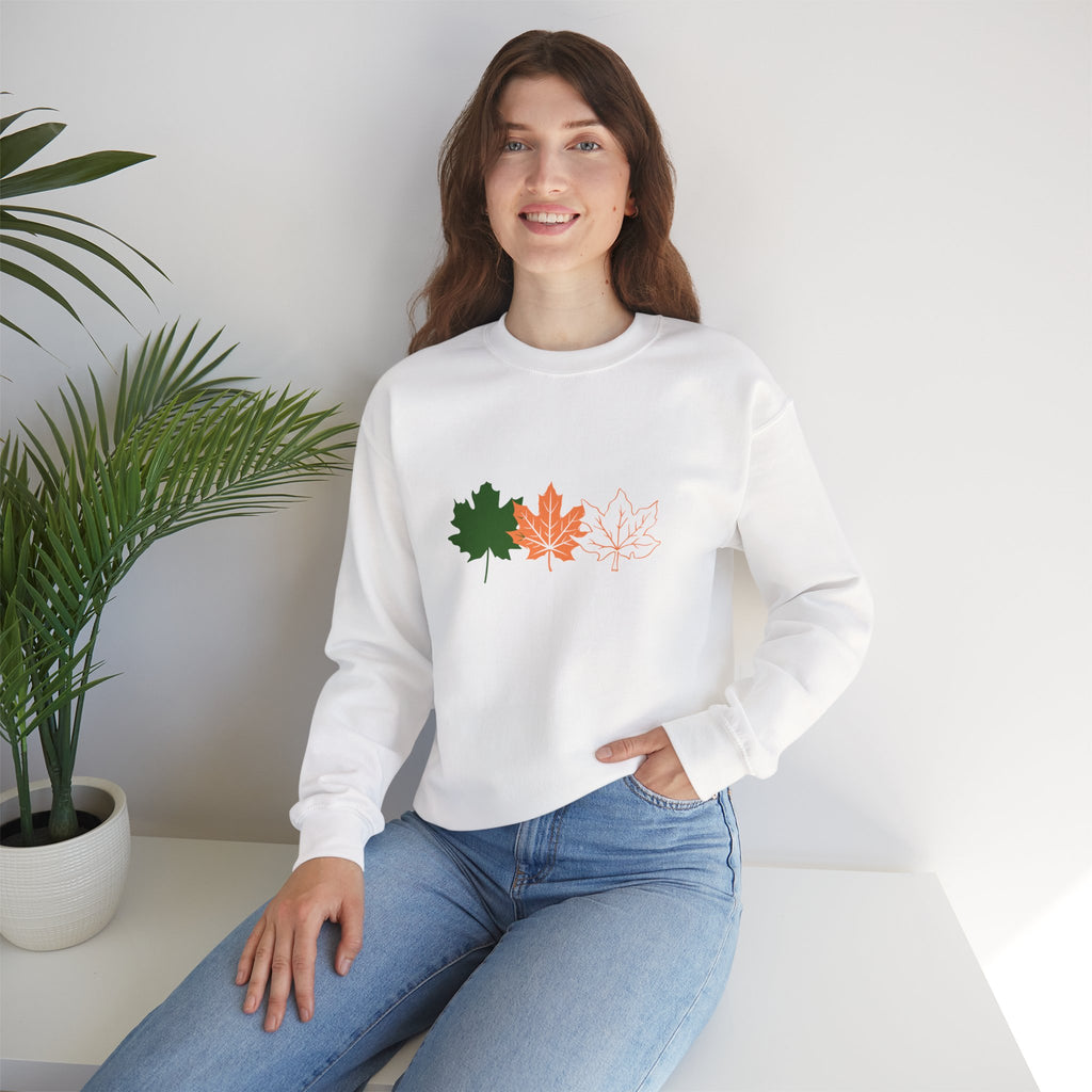 Woman wearing a white sweatshirt with leaf designs sitting in a room with a plant.