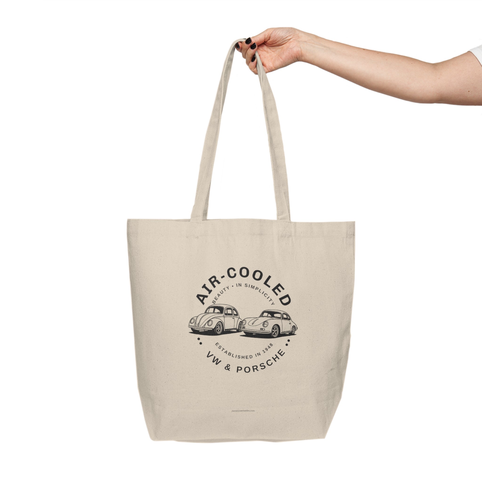 Beige tote bag with car design and text held by a hand on a white background