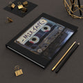 Notebook with a cassette tape design on the cover, surrounded by office supplies on a dark surface.