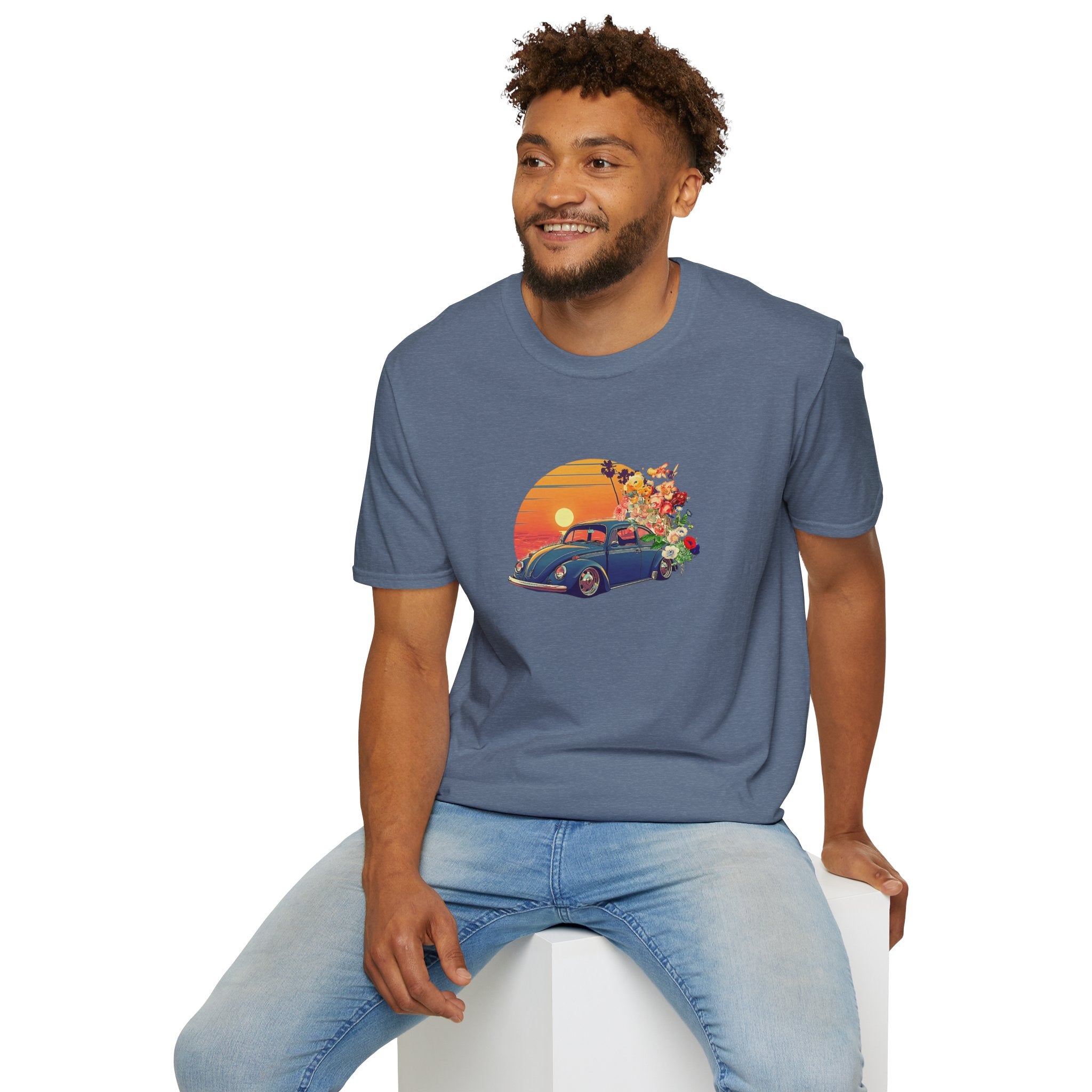 Man wearing a blue t-shirt with a graphic design of a car and sunset, sitting on a white stool against a white background.