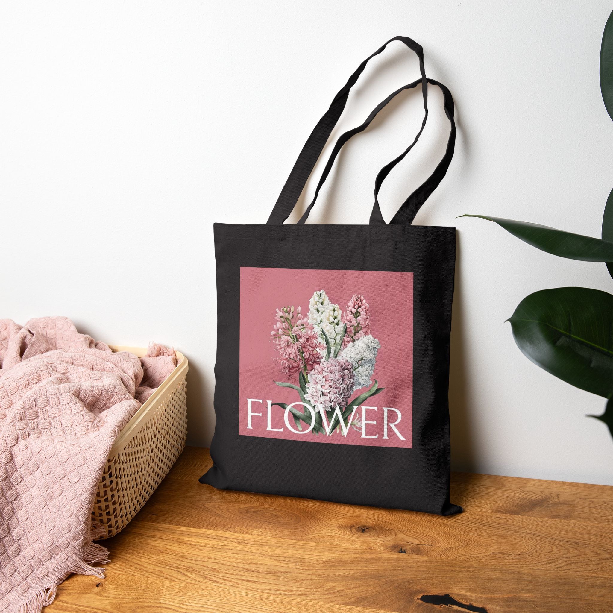 Black tote bag with floral design and 'FLOWER' text on a wooden surface.