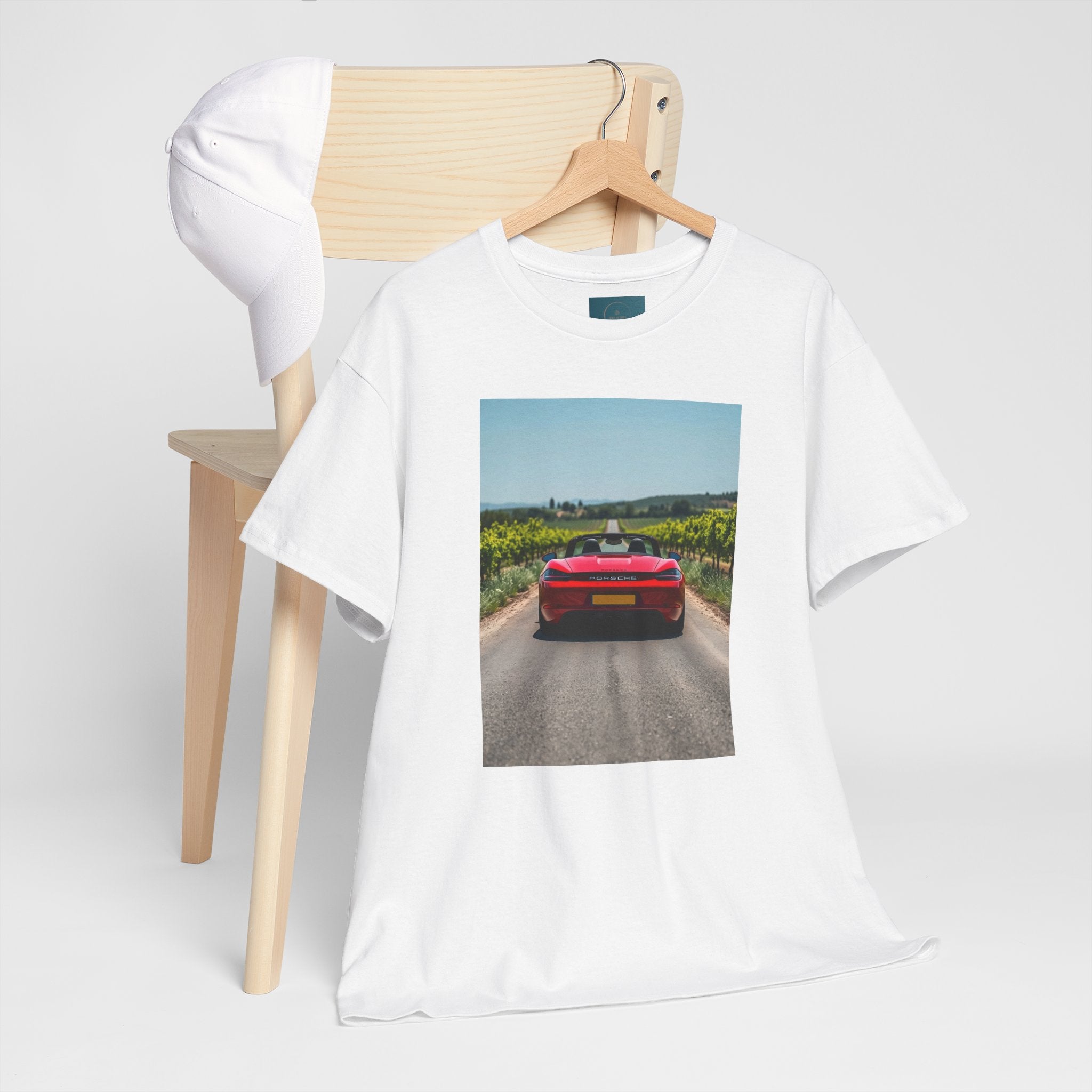 White t-shirt with a printed design of a porsche on a road, hanging on a wooden chair.