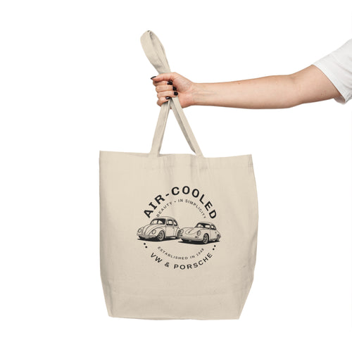 Beige tote bag with VW and Porsche logo held by a hand on a white background