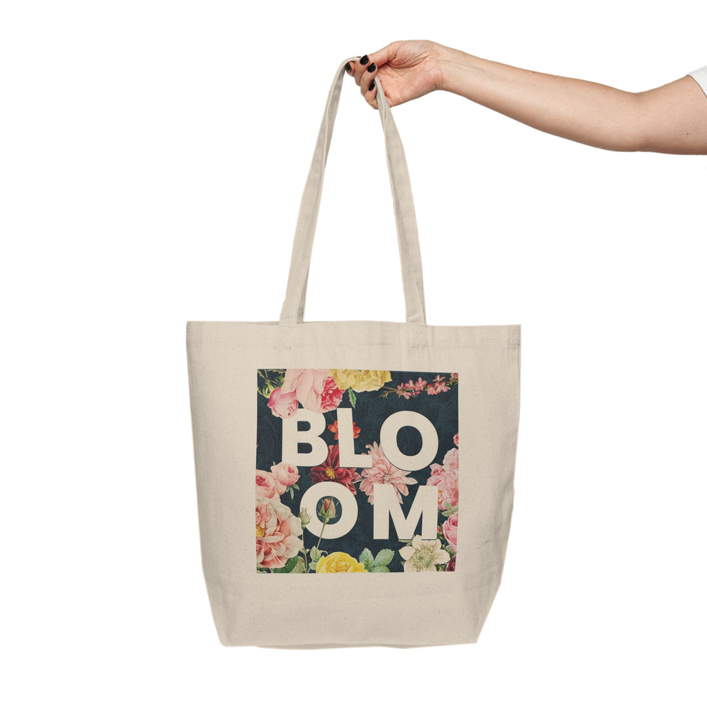 Tote bag with 'BLOOM' text and floral design held by a hand on a white background