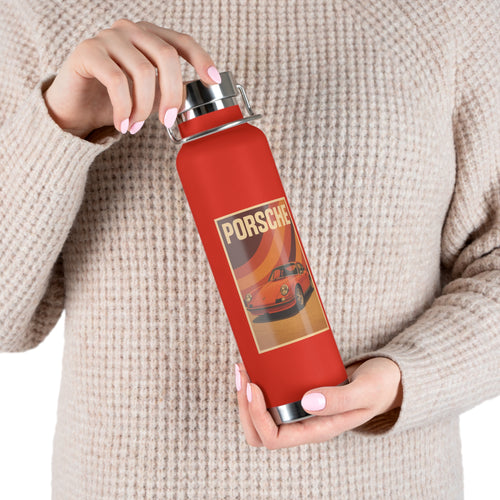 Red water bottle with Porsche design held by a person wearing a beige sweater.