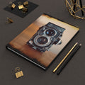 Notebook with vintage camera design on a dark surface with office supplies.
