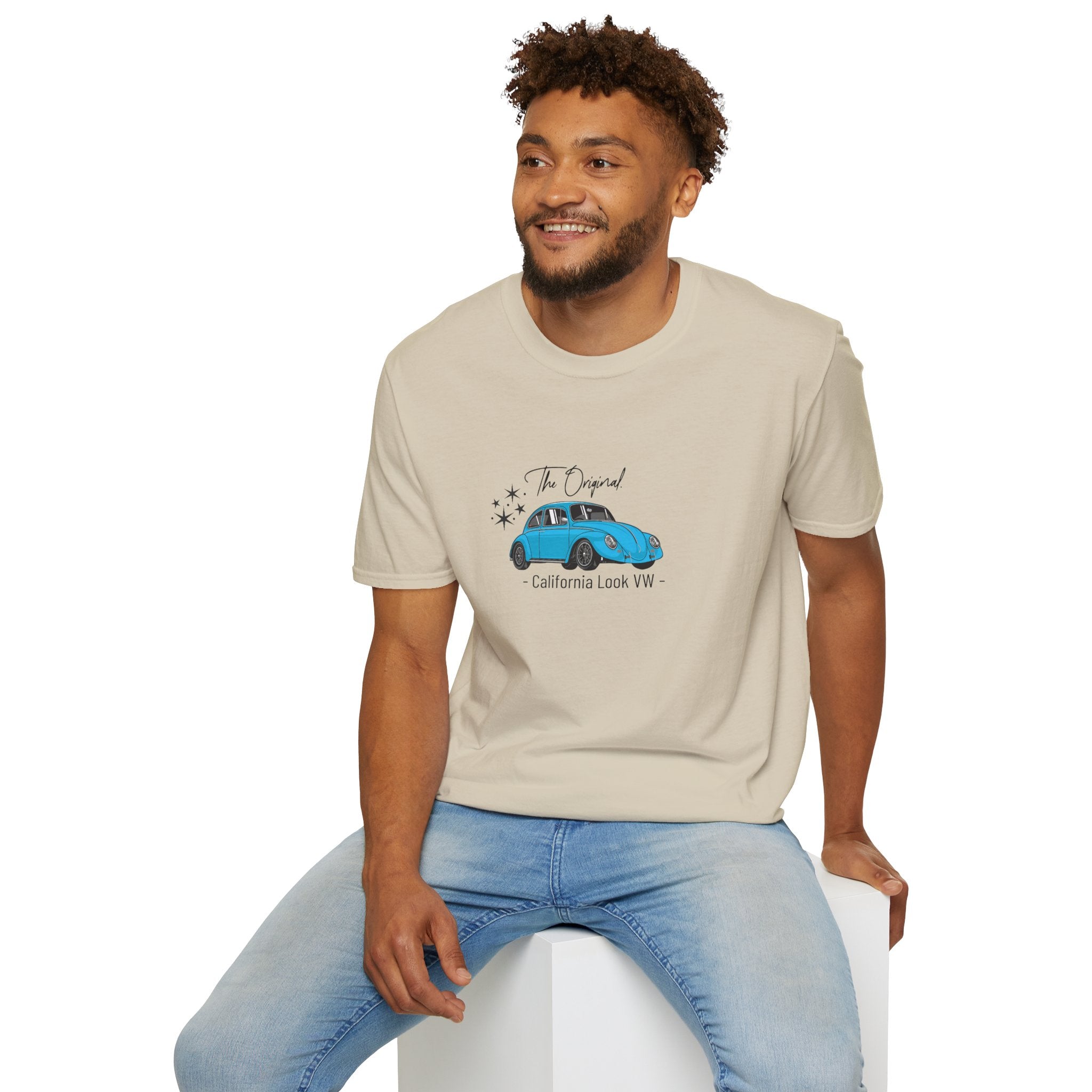 Man wearing a beige t-shirt with a blue vw beetle graphic and text, sitting on a white stool against a white background.