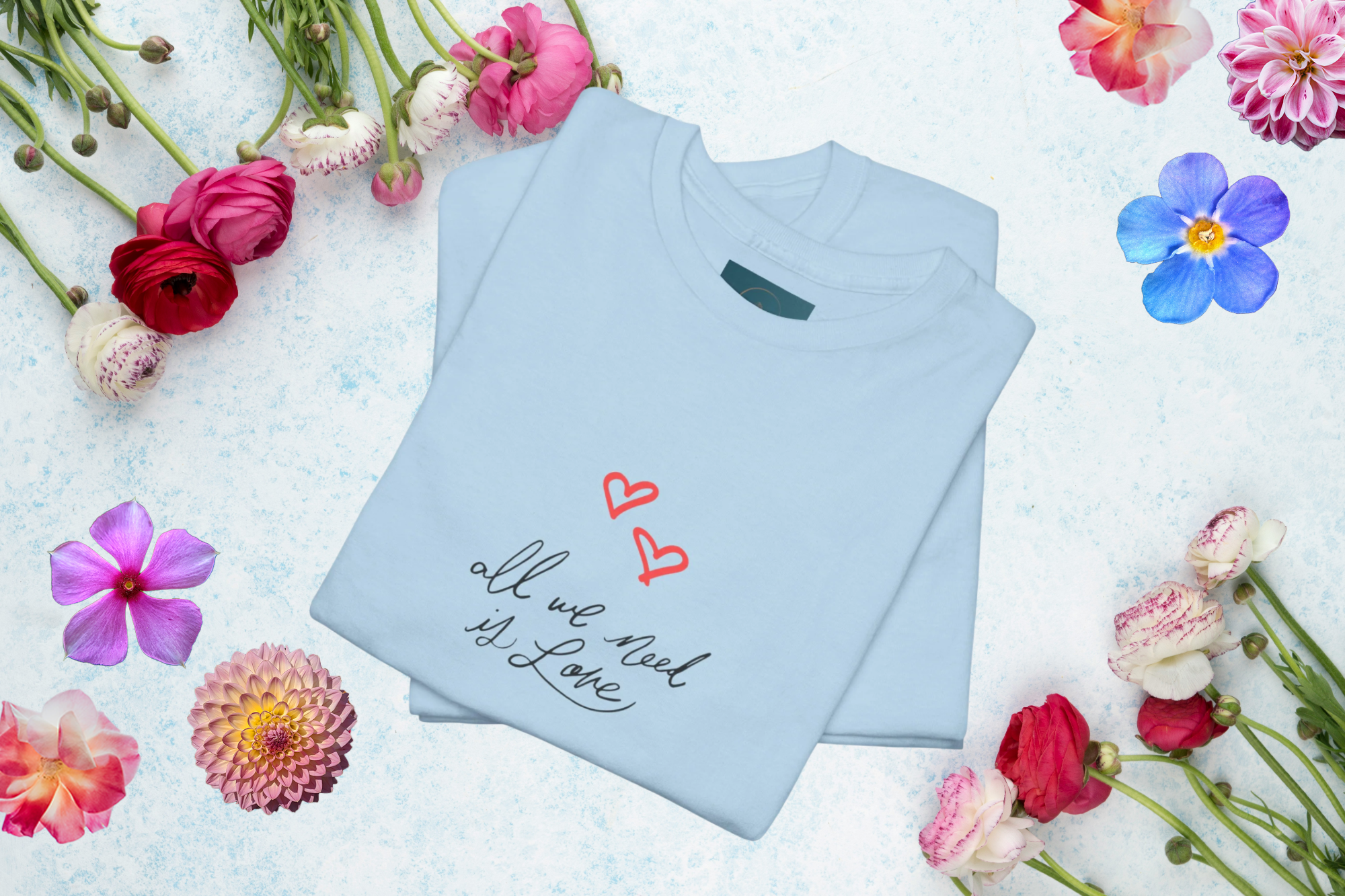 Light blue t-shirt with 'all we need is love' text and hearts on a floral background