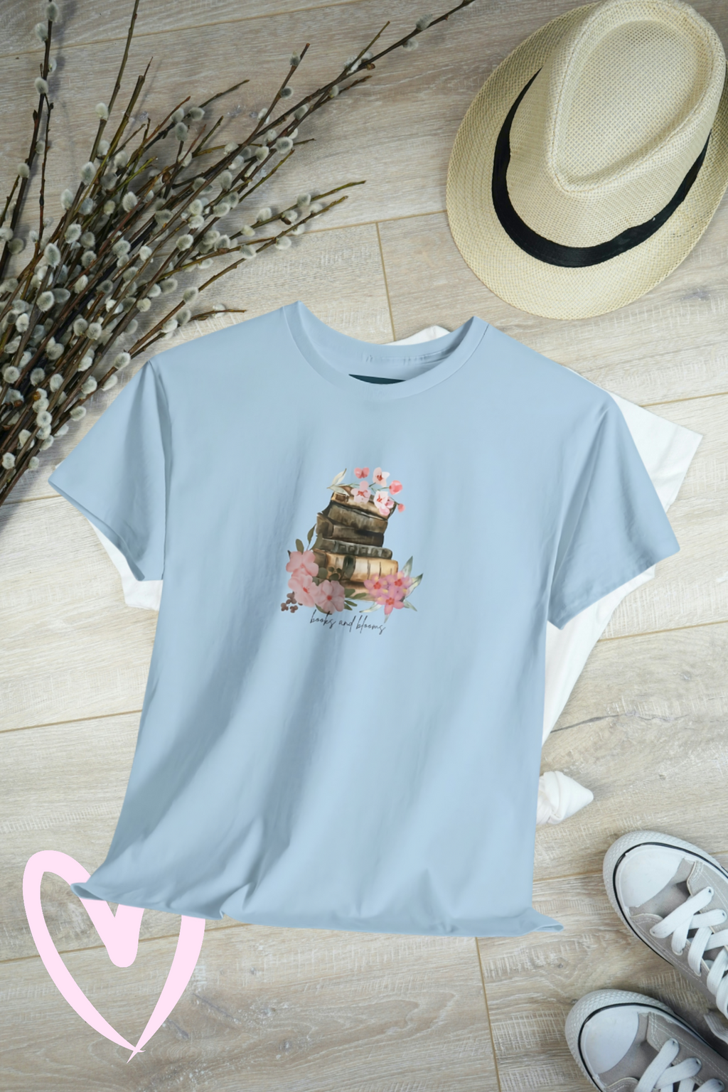 Light blue t-shirt with a books and blooms design on a wooden surface with a hat and shoes.