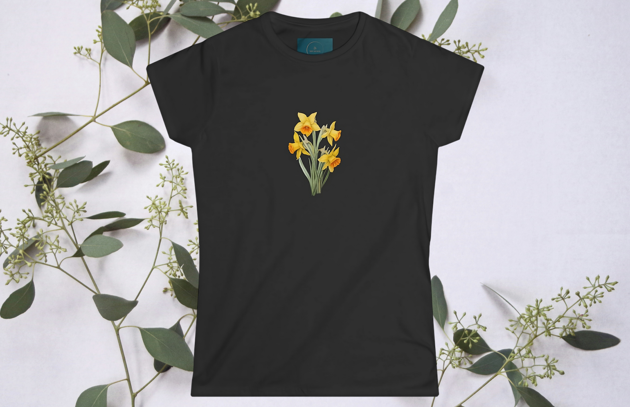 Black t-shirt with yellow daffodil flower design on a white background with green leaves.