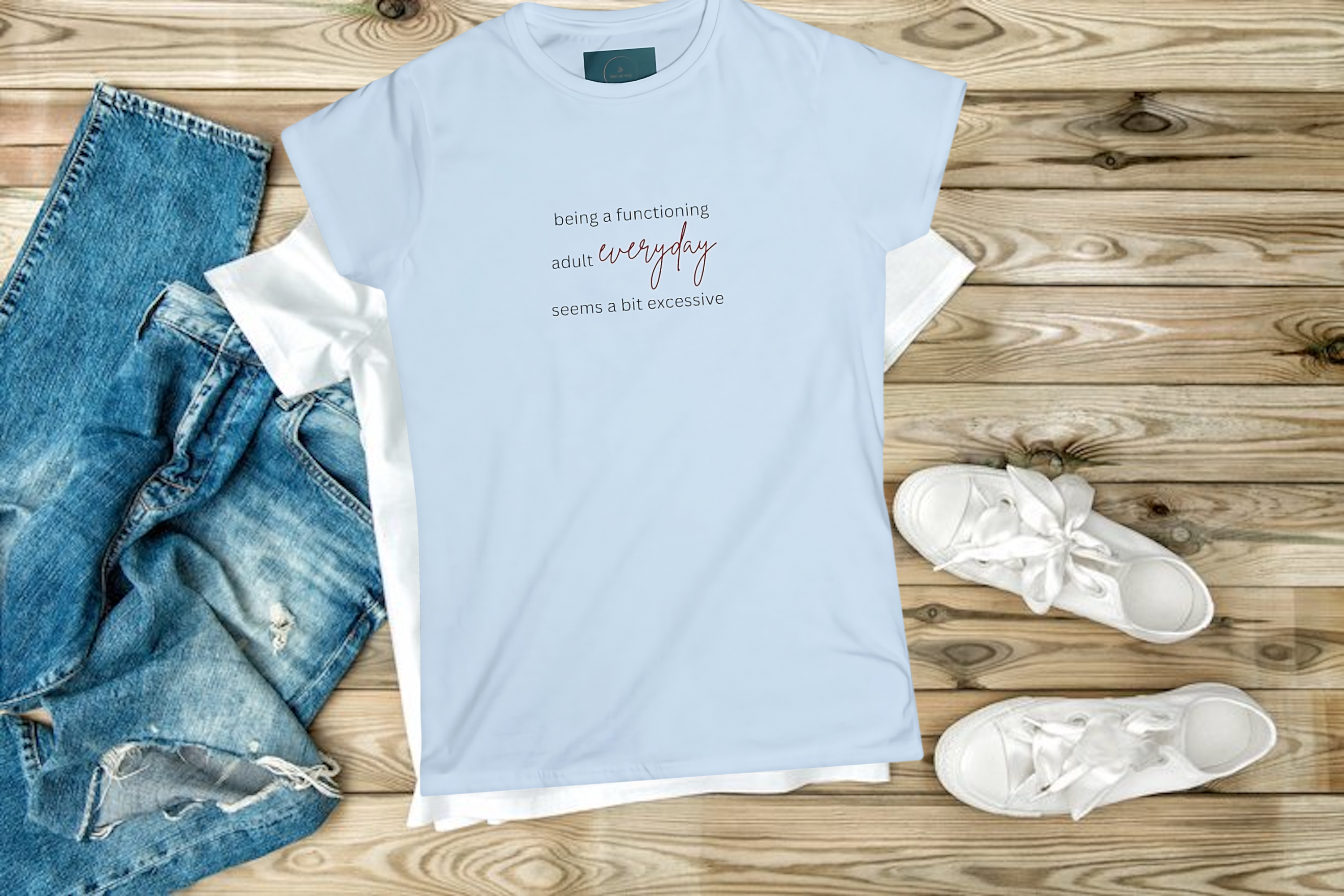 Light blue t-shirt with text, jeans, and white sneakers on a wooden surface
