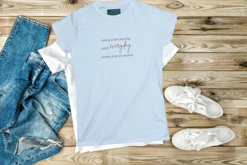 Light blue t-shirt with text, jeans, and white sneakers on a wooden surface