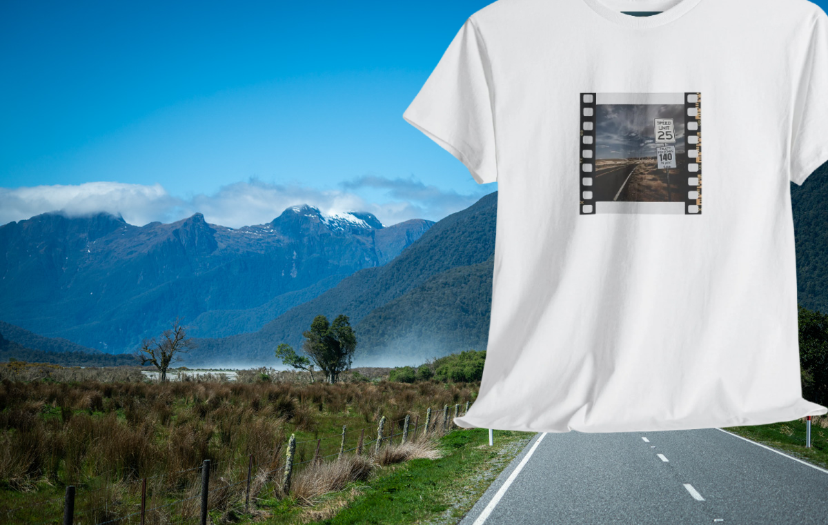 White t-shirt with a film strip design featuring a scenic road and mountains, set against a scenic backdrop.