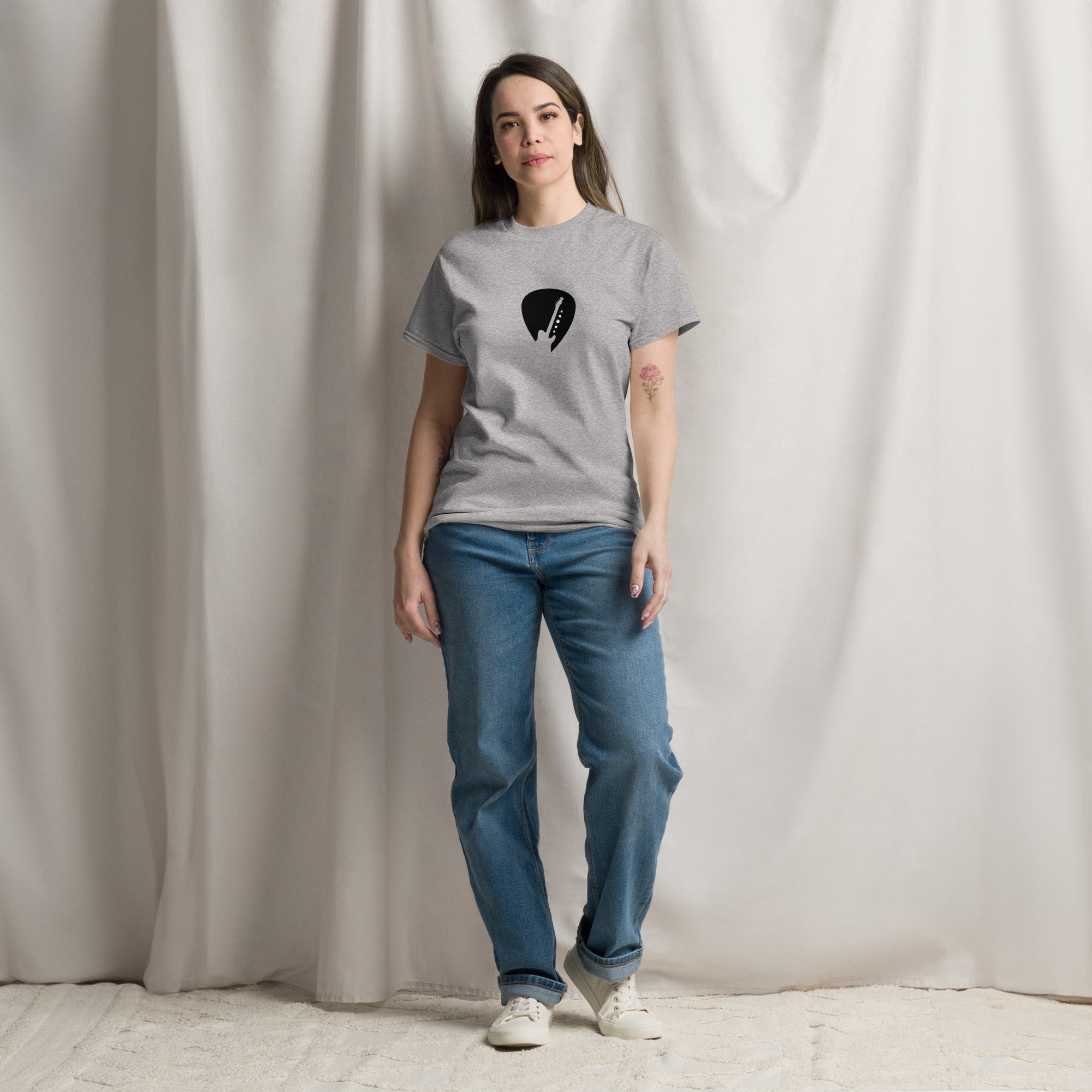 Woman wearing a gray t-shirt with a black graphic design and blue jeans against a plain background