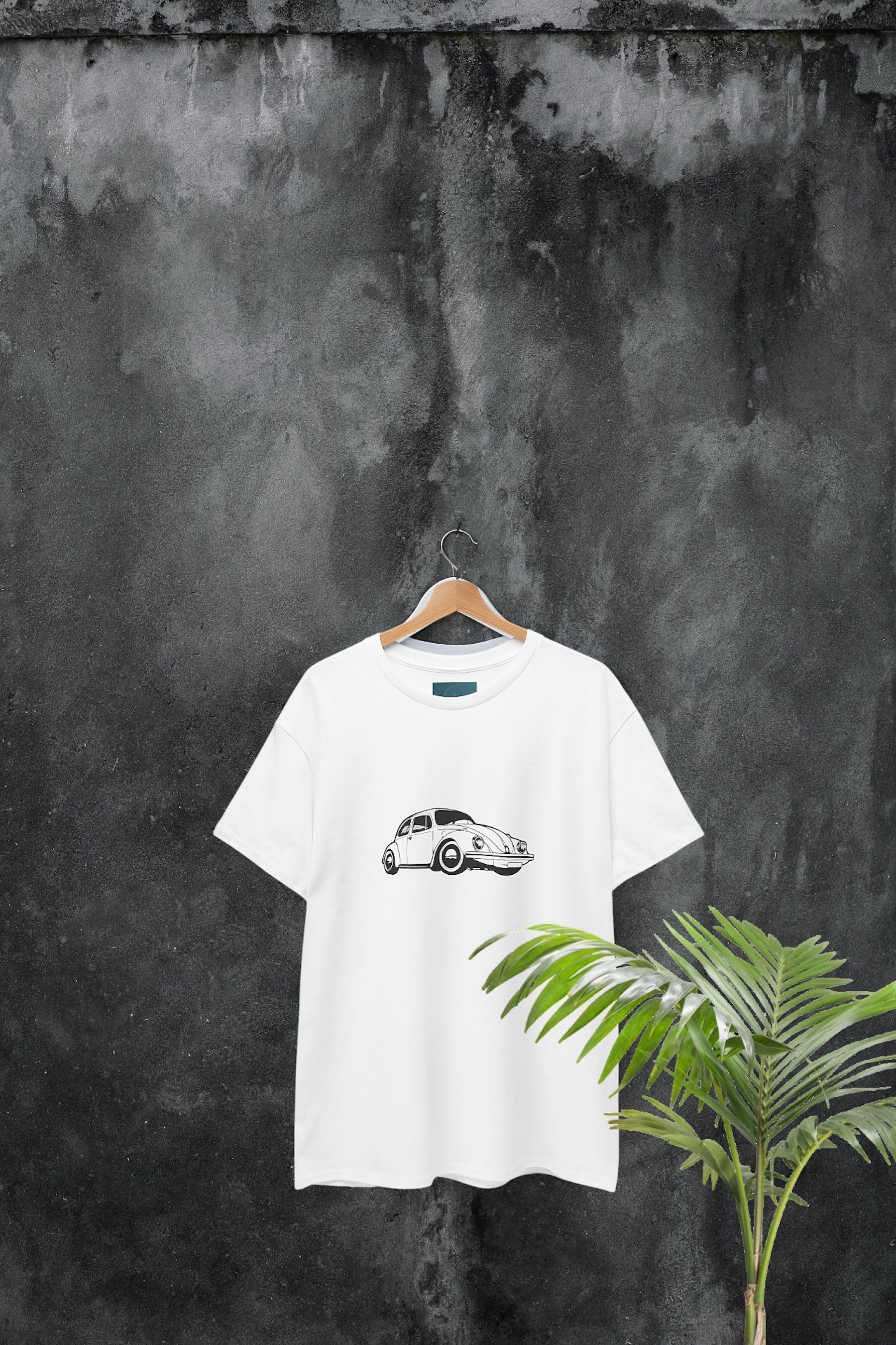 White t-shirt with a black vw beetle graphic on a hanger against a textured dark wall.