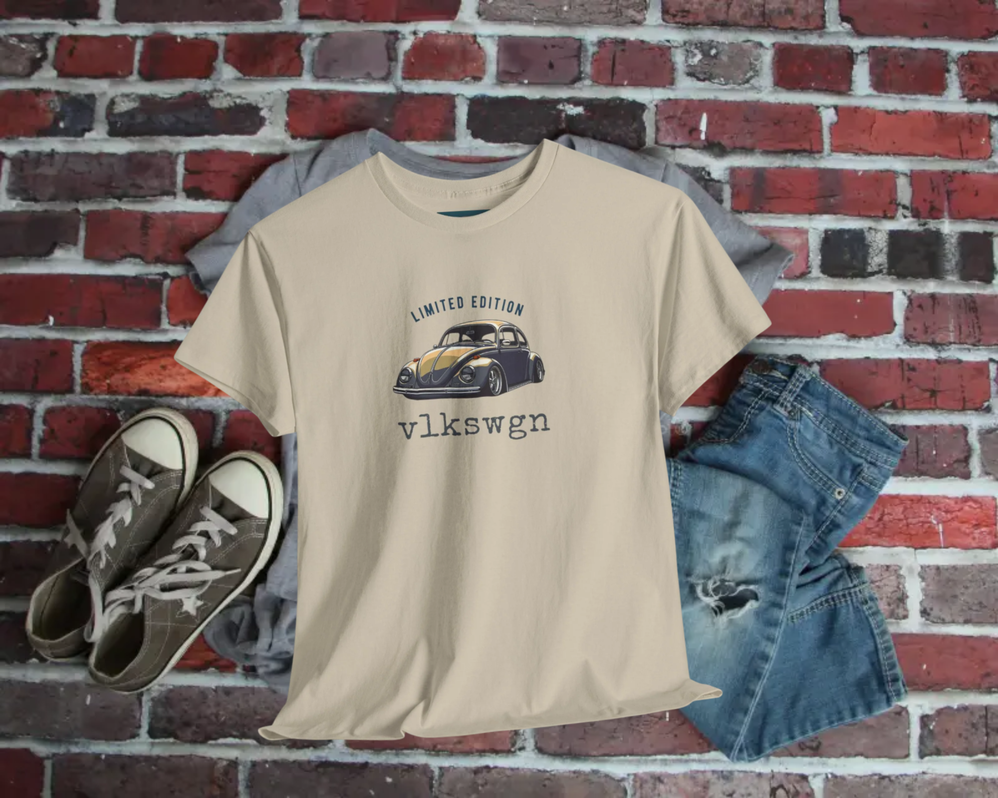 Beige t-shirt with Volkswagen beetle graphic, placed on a brick wall with shoes and shorts.
