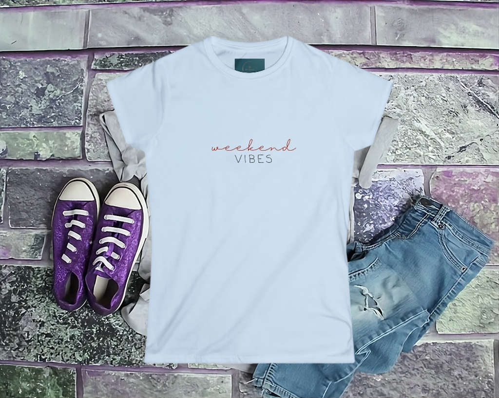White t-shirt with 'weekend vibes' text, purple sneakers, and denim shorts on a stone surface.